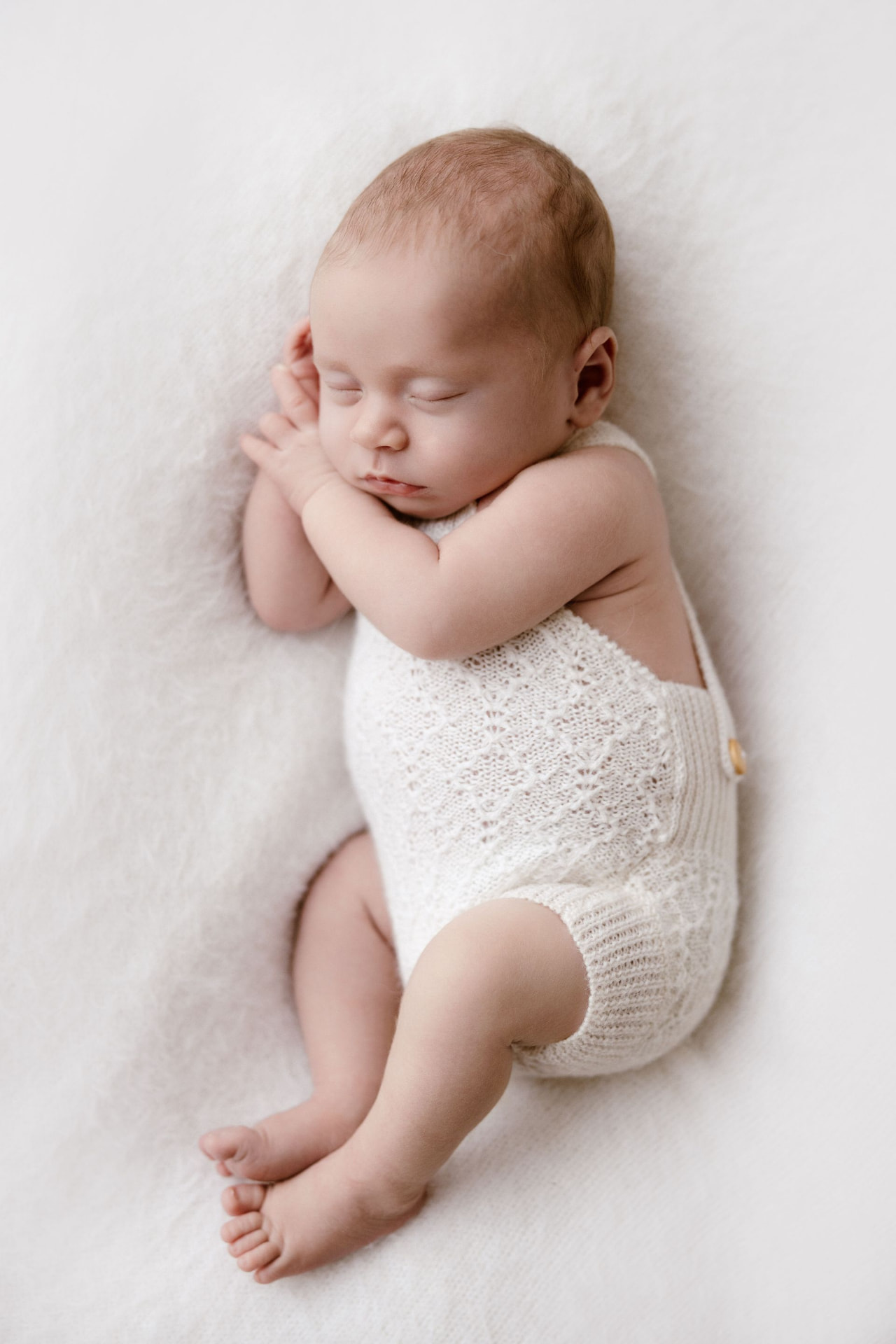 Newborn asleep on her back in a white knitted romper