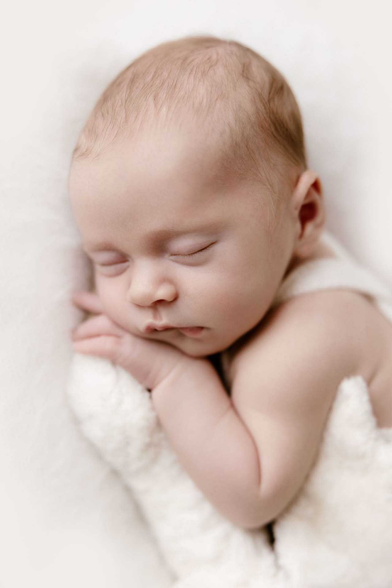 Close up of a sleeping newborn resting her cheek on her hands