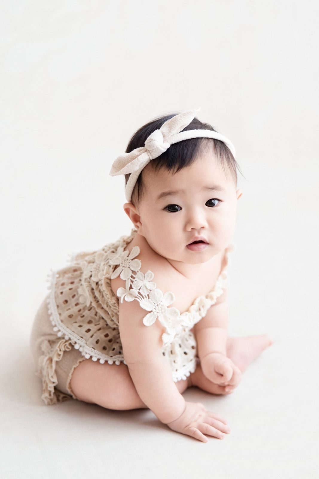 Baby girl sitting up in a lace romper and bow