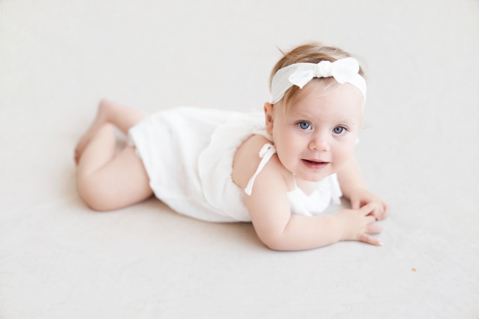 Smiling baby on her tummy in a white romper