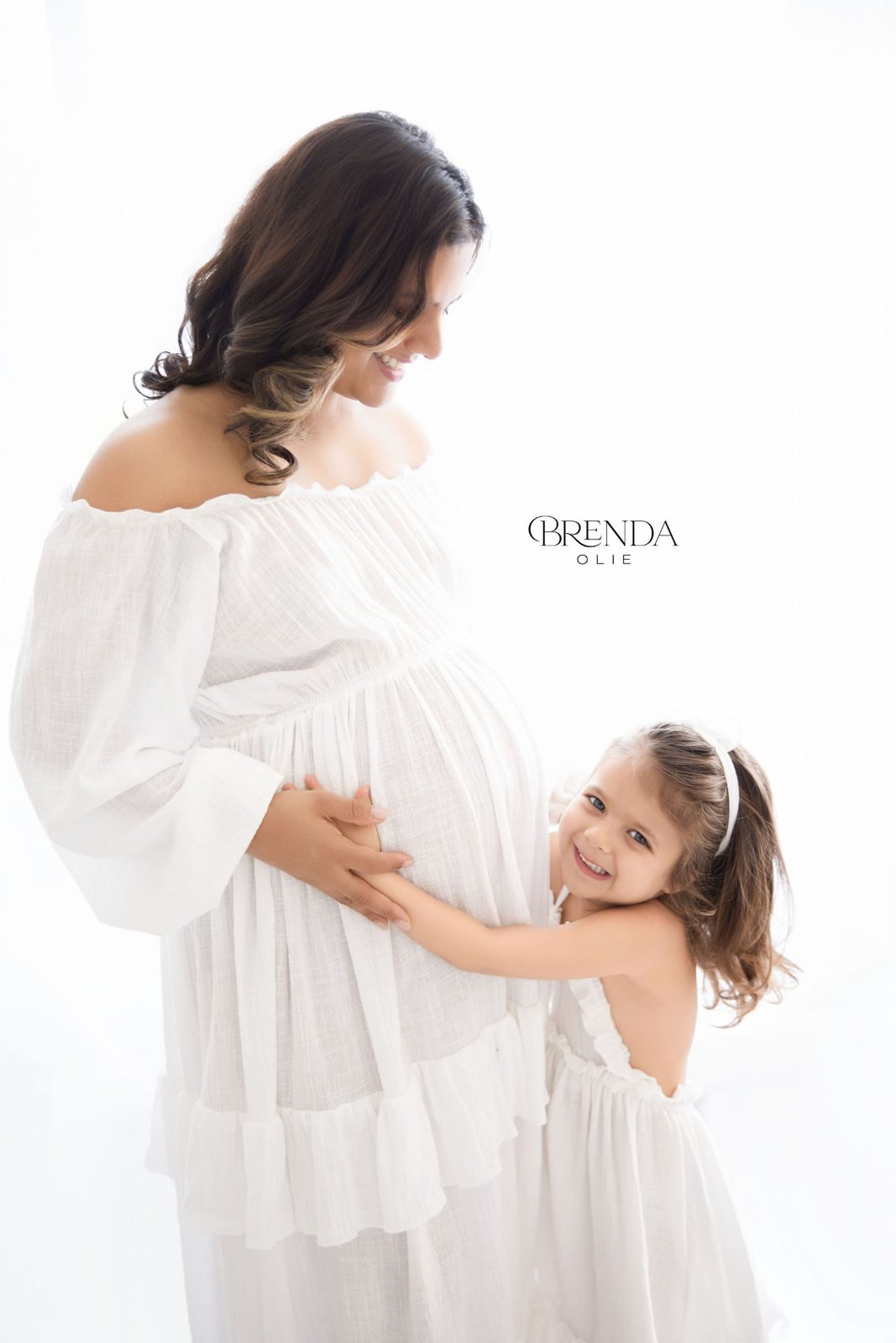 Little girl hugging her mother's baby bump and smiling at the camera
