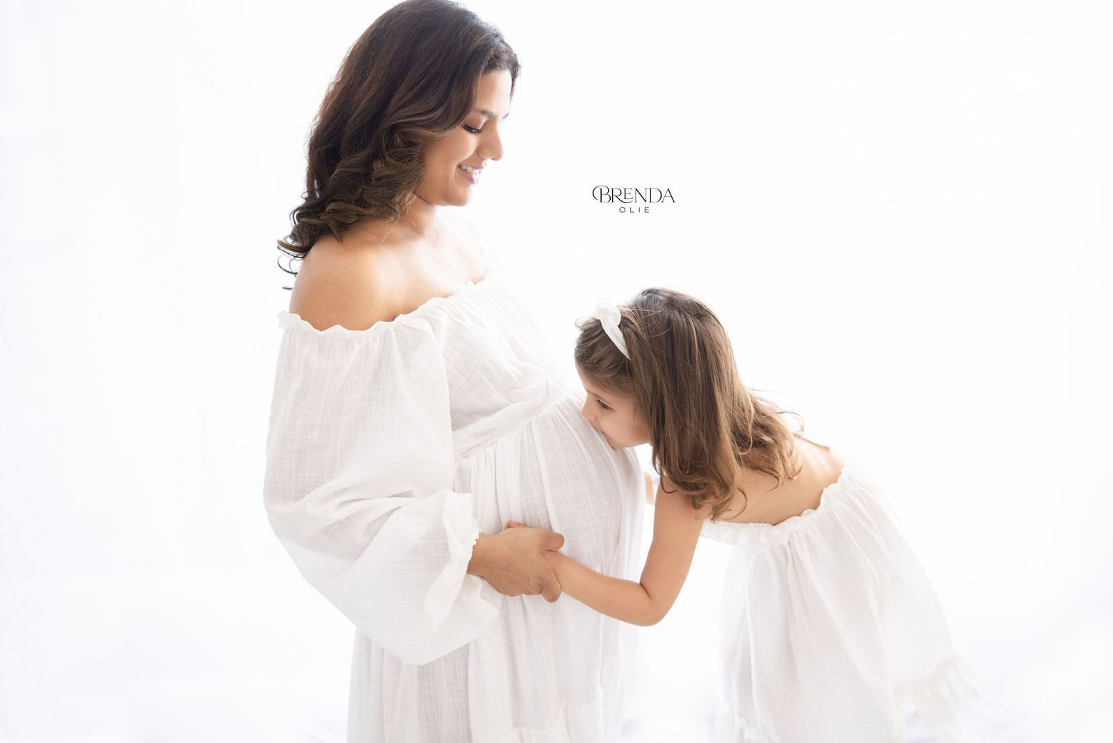 Expecting mother holding her little girl close while they smile at each other