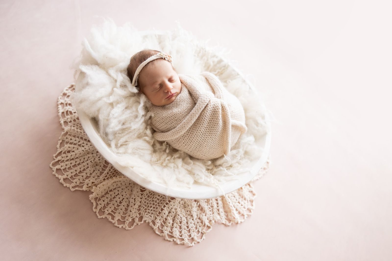 Wrapped newborn posed in a white bowl on lace