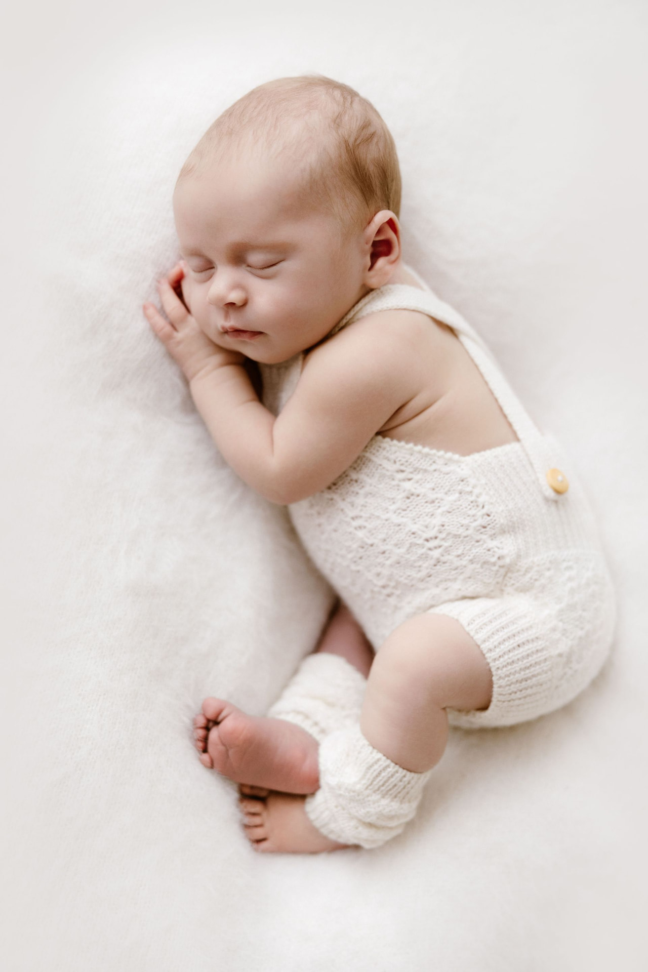 Newborn curled up asleep in a knitted romper