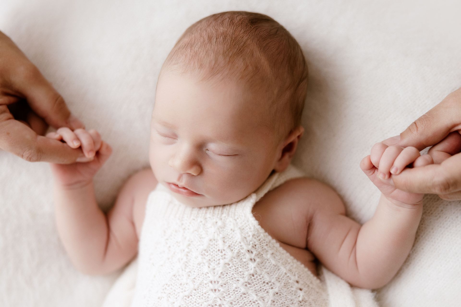 Newborn's hands held by her parents