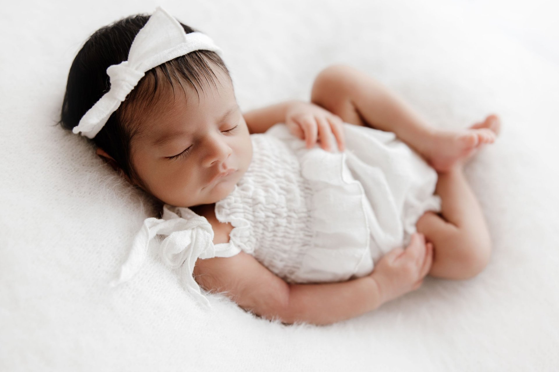 Newborn girl asleep in white with a linen bow